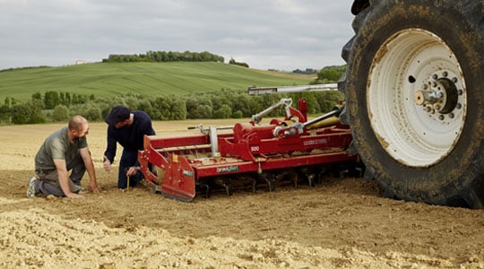 Un agriculteur accroupi tient de la terre dans ses mains